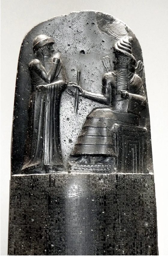 The upper section of the basalt Code of Hammurabi stele: a standing figure before a seated deity, above dense columns of cuneiform.
